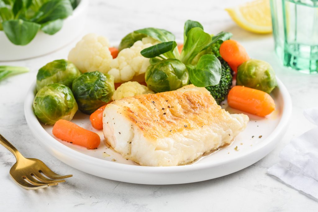 Cod with vegetables on a dinner plate.