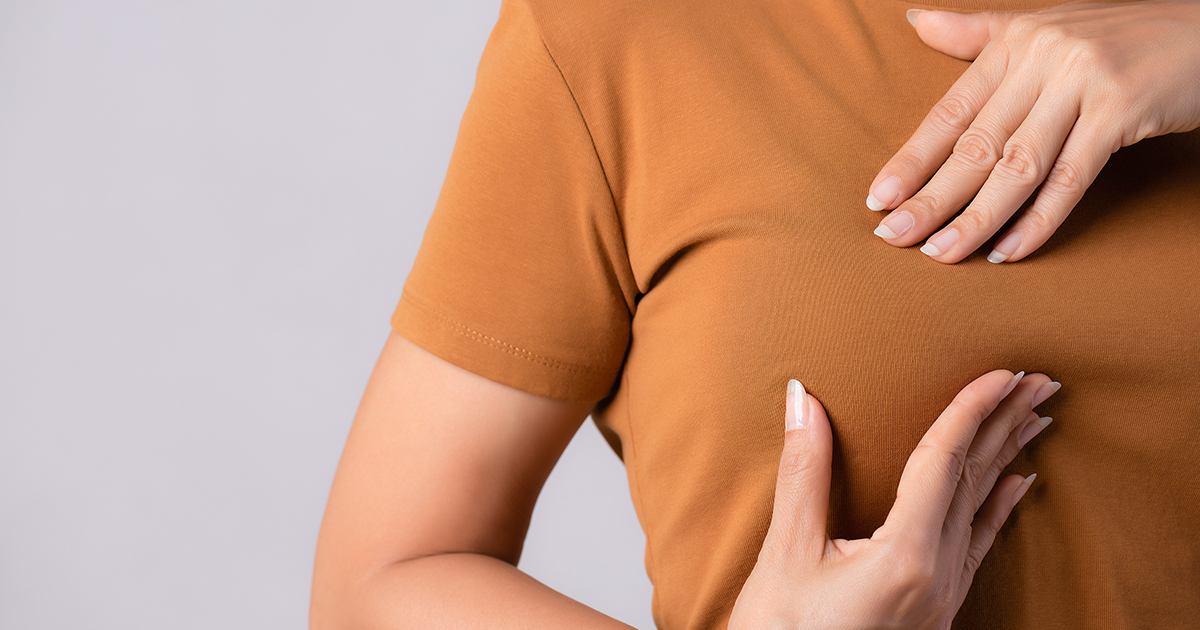 Woman hand checking lumps on her breast for signs of breast cancer.